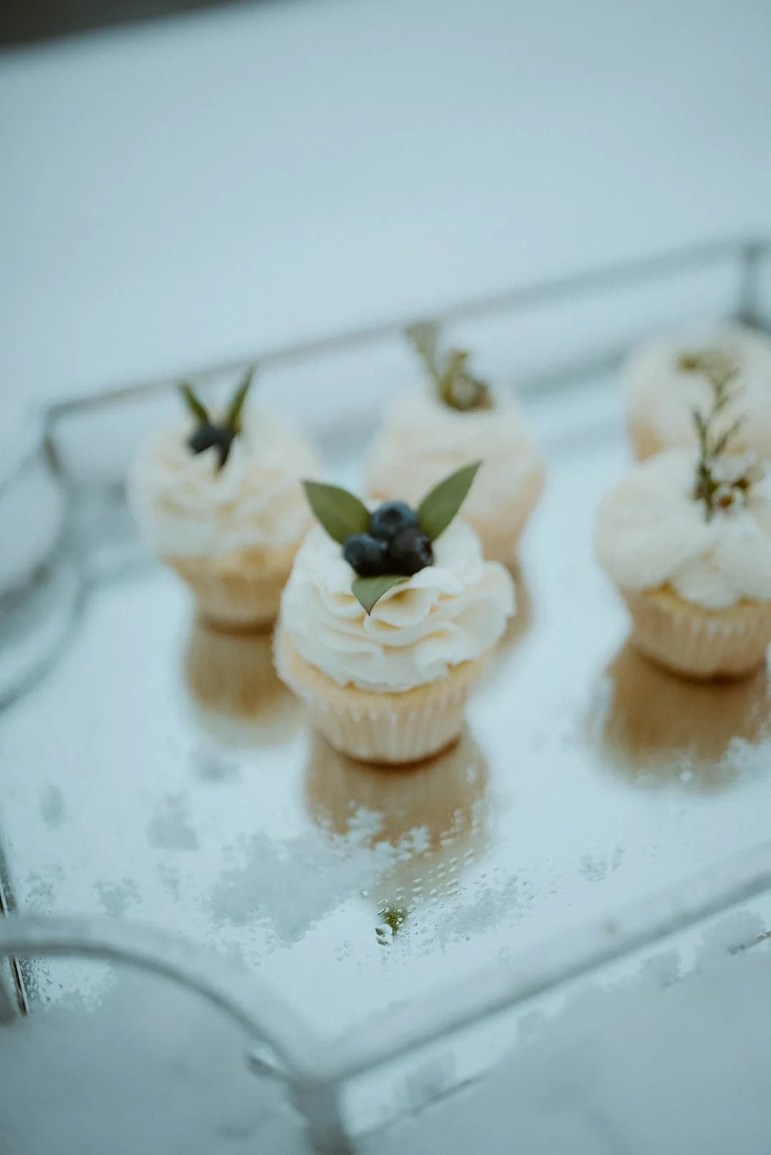 Mini vanilla cupcakes with blueberries on a mirrored tray
