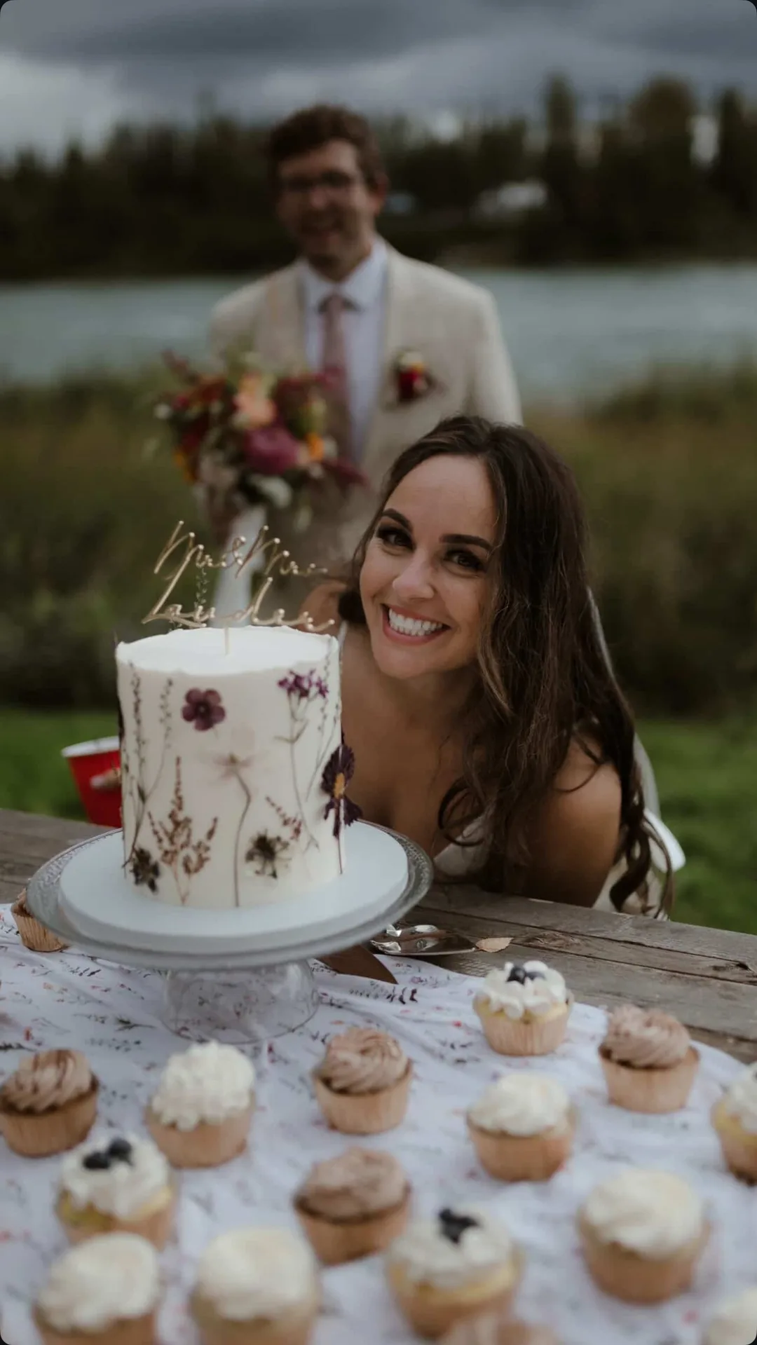 Bride smiling beside her pressed-flower wedding cake