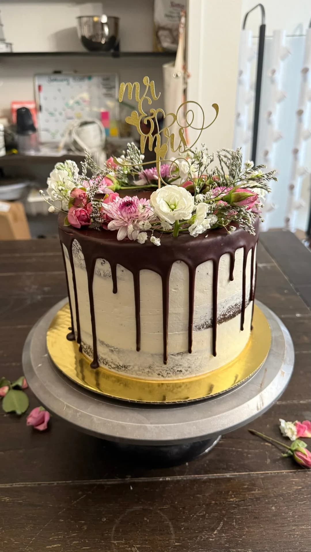 Chocolate drip cake topped with fresh pink flowers