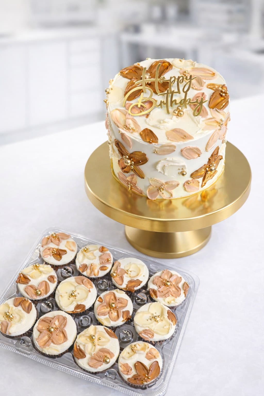 White birthday cake with gold and blush brushstrokes on a gold stand