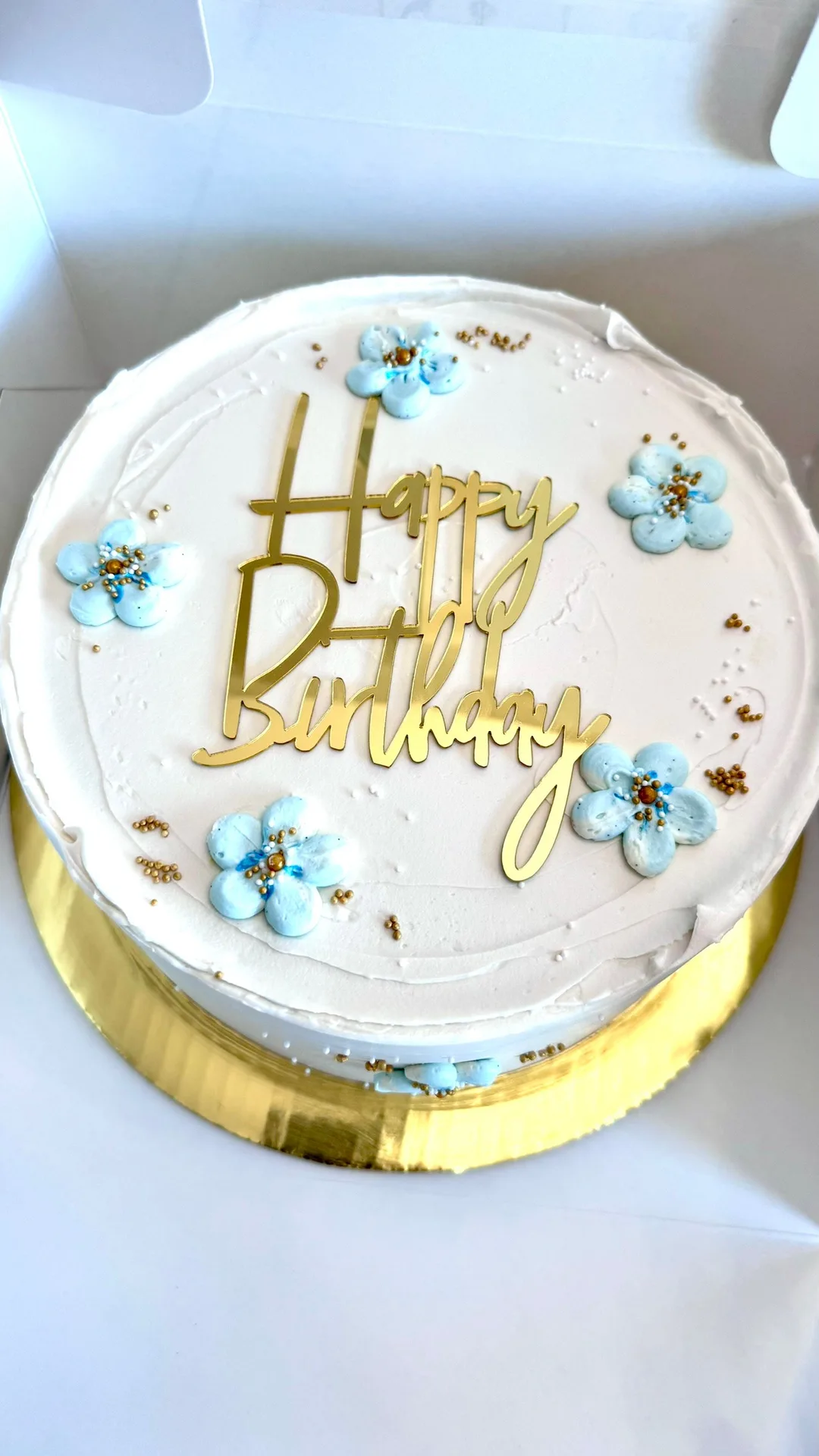 White birthday cake with blue piped blossoms and gold topper