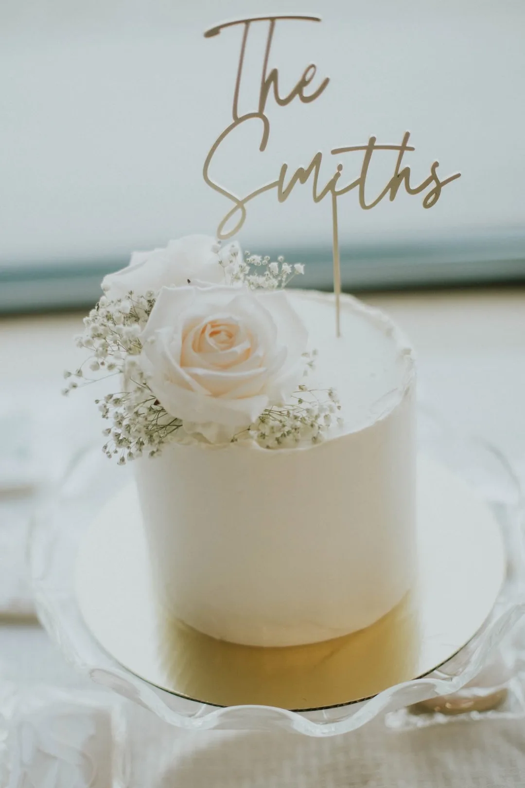 Minimal white wedding cake with a single blush rose and gold name topper