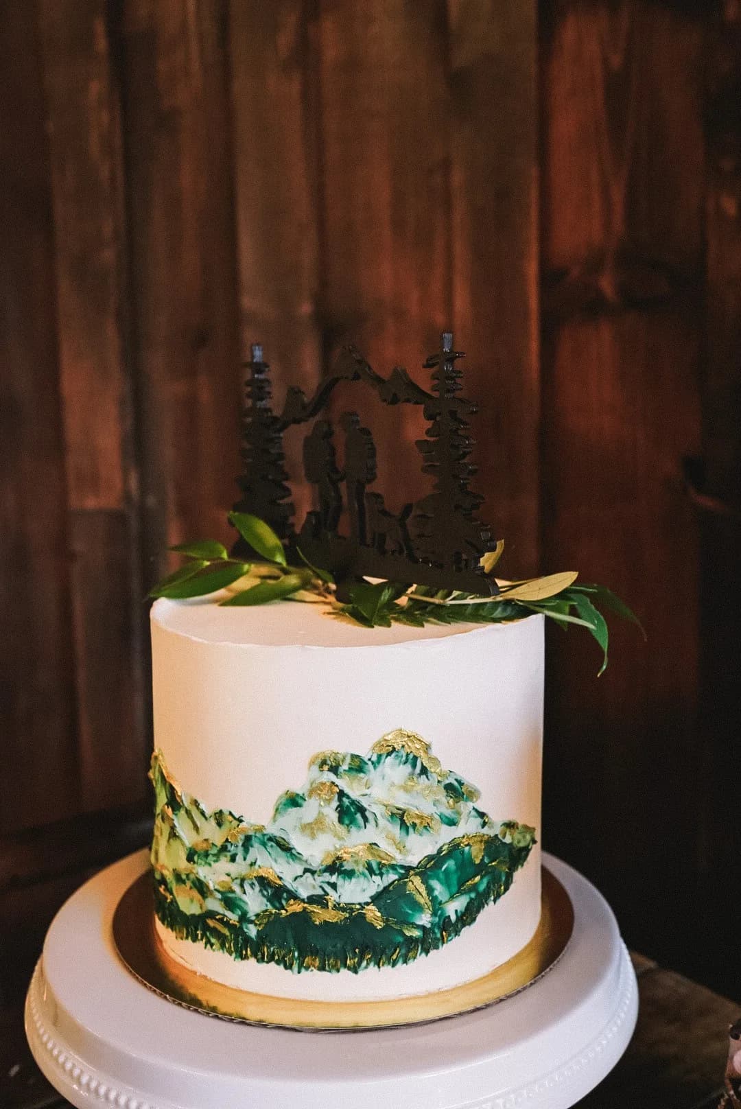 White wedding cake with painted buttercream mountains and a forest topper
