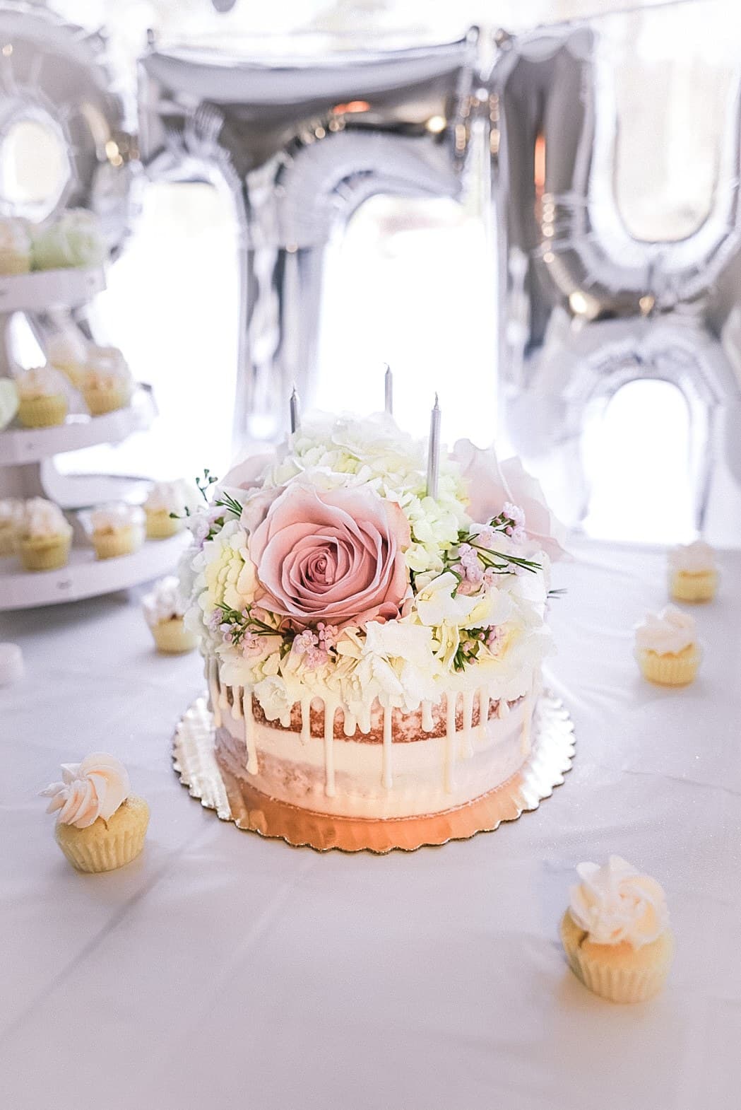 Pink drip wedding cake with dusty roses and mini cupcakes