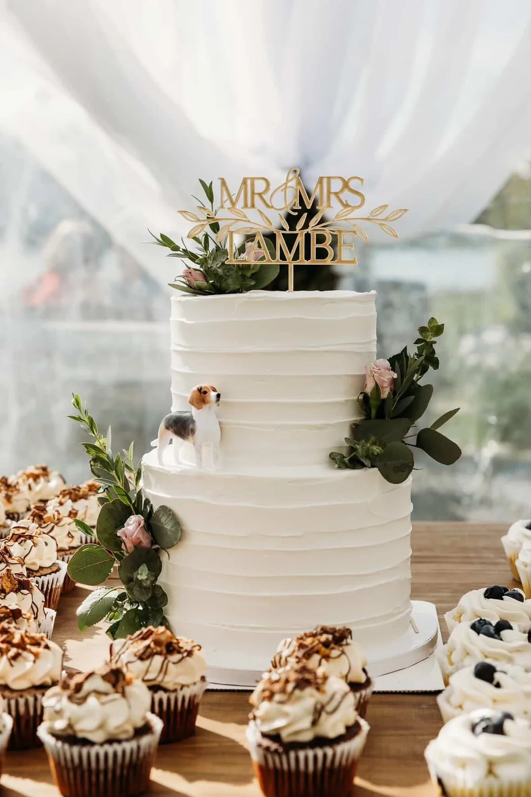 Ribbed buttercream wedding cake with greenery and a tiny dog topper